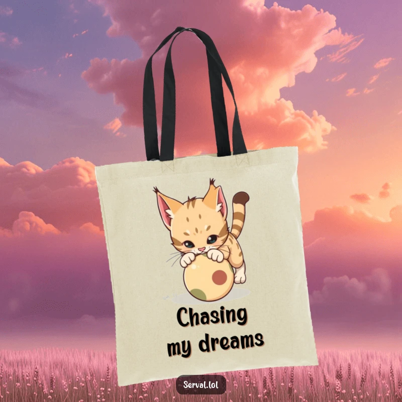 Funny Serval Pounce Tote Bag. A serval cat playfully pounces on a rolling ball, making this bag a humorous and stylish accessory.